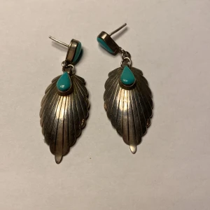 Silverörhängen Navajo med turkos detalj  - Snygga vintage Navajo silverörhängen tillverkade i USA , formade som löv med en turkos droppe på toppen. Perfekta för att ge en bohemisk touch till din stil. De har en elegant och unik design som drar blickarna till sig. 