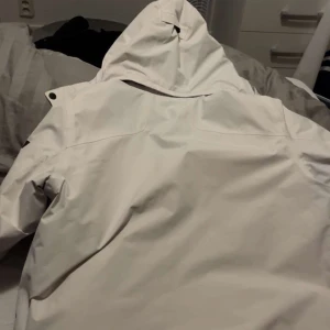 Vit vinterjacka från Sail racing - Säljer en vit vinterjacka från Sailracing med huva och flera fickor. Jackan har dragkedja och knappar framtill samt svarta detaljer. Jackan har använts en gång säljer den pågrund av att den inte passar längre. Pris kan diskuteras. Perfekt för kalla dagar!