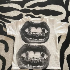 Vit t-shirt med tryck av tänder - Cool vit t-shirt med ett stort tryck av tänder i svart. Perfekt för en unik och edgy stil. Kortärmad och i bomull för en bekväm passform.