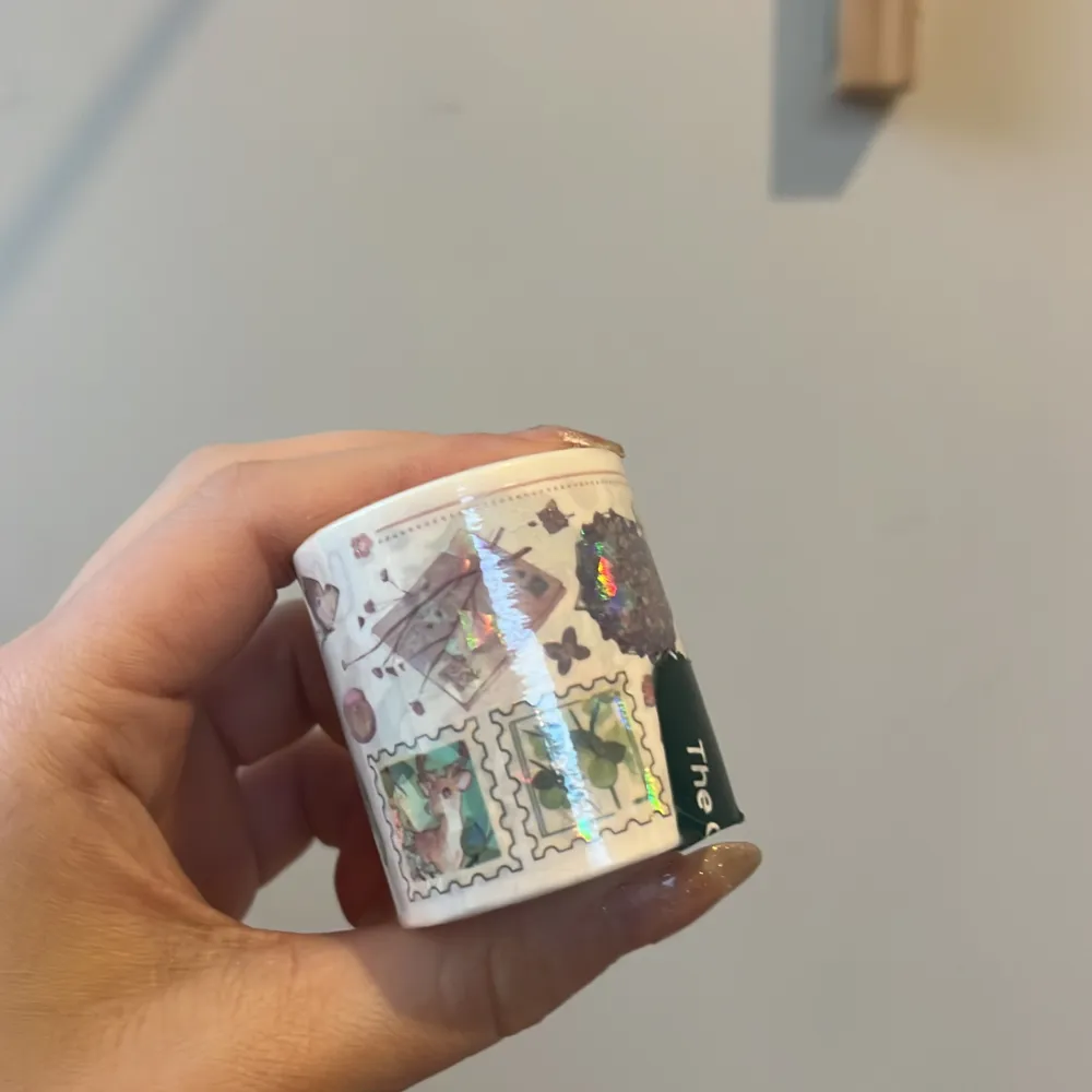 Säljer en rulle dekorativ tejp med ett färgglatt anime-motiv. Tejpen har en vit bas med illustrationer av en karaktär med långt blått hår och olika små detaljer som ger en lekfull känsla. Perfekt för att dekorera anteckningsböcker eller paket.. Asusteet.