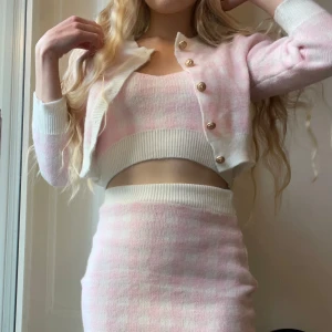 Stickat set  - Rosa rutigt gulligt set som består av ett linne, kofta och en minikjol! Superfint att kombinera eller mixa och matcha. Endast använt ett fåtal gånger                                                                 Mått på toppen: Byst: 80-90 Längd: 40 Mått på koftan: Axlar: 35 Byst: 92 Längd:42 Mått på kjolen: Midja: 62-76 Längd: 46 