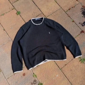 Svart tröja från Yves Saint Laurent - Snygg svart tröja från Yves Saint Laurent med vita detaljer vid hals och ärmslut. Den har en broderad logotyp på bröstet och är perfekt för en stilren look.