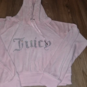 Rosa hoodie från Juicy Couture - Säljer en söt rosa hoodie från Juicy Couture med glittrande stenar som bildar texten 'Juicy' på framsidan. Hoodien har en justerbar dragsko i huvan och långa ärmar. Perfekt för en avslappnad stil.