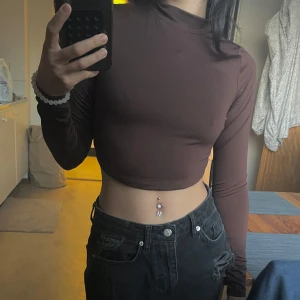 Brun långärmade croppad topp - Säljer en brun croppad polotopp med långa ärmar. Perfekt för en trendig och stilren look. Passar bra till både jeans och kjol. Från nelly och har knappt blivit användt. Stretchy material.