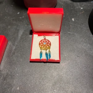 Halsband med drömfångarhänge - Unikt halsband med ett drömfångarhänge i guld och blått. Hänget har en intrikat design med blå fjädrar och en central pärla. Använd endast 2 gånger