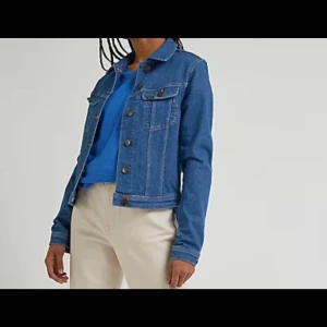 Blå jeansjacka från Lee - Säljer en klassisk blå jeansjacka från Lee i storlek L. Jackan har knappar framtill och två bröstfickor med knappstängning. Tillverkad i ekologisk bomull för en hållbar stil.