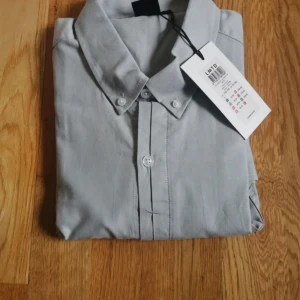 Grå skjorta från LMTD - Snygg grå skjorta från LMTD i storlek 170-176. Skjortan har en klassisk krage och knappar framtill. Perfekt för en stilren look.
