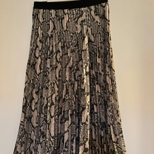 Ormmönstrad kjol - Snygg ormmönstrad kjol med plisserad design. Kjolen har en elastisk midja för bekväm passform och ett trendigt mönster i svart och beige. Perfekt för att ge din outfit en edgy touch.