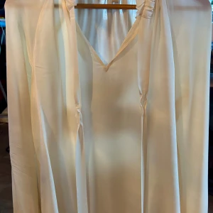 Beige klänning från Michael Kors - Elegant beige blus från Michael Kors med v-ringning och knytband vid halsen. Perfekt för en stilren look.