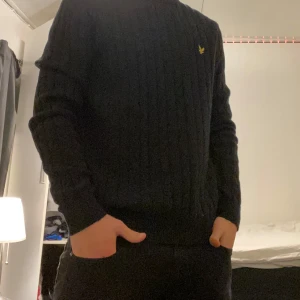 Svart kabelstickad tröja från Lyle & Scott - Säljer en stilren svart stickad tröja från Lyle & Scott med deras ikoniska logga på bröstet. Tröjan har en ribbad design och långa ärmar, perfekt för kyligare dagar. Passar både till vardags och mer uppklädda tillfällen. Pris går att diskuteras. Storlek M. 