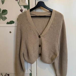 Beige stickad kofta från Gina Tricot - Säljer en mysig beige stickad kofta från Gina Tricot. Koftan har en v-ringad design med knappar framtill och långa ärmar. Perfekt för kyliga dagar!
