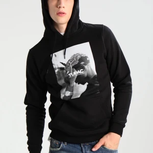 Svart hoodie med Tupac-tryck (pris kan diskuteras) - Snygg svart hoodie med ett stort tryck av Tupac på framsidan. Perfekt för dig som vill ha en bekväm och stilren tröja med en ikonisk design. Hoodien har en klassisk passform och en praktisk ficka framtill.