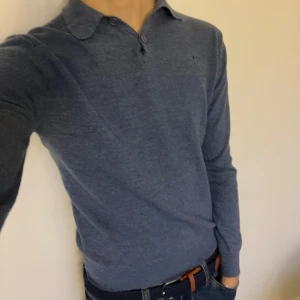 Blå pikétröja från Morris - Säljer en stilren blå pikétröja från Morris i storlek M och som är i fint merinoull. Tröjan har en klassisk krage med knappar och ett diskret broderat emblem på bröstet. Perfekt för en avslappnad men ändå elegant look. Den är i storlek M men sitter mer som en s, den passar 174cm till ca 180. Modellen är 180