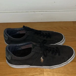 Polo Ralph Lauren skor - Svarta sneakers från Polo med snörning och vit sula. Skorna har en broderad logotyp på sidan och är tillverkade i syntetmaterial.