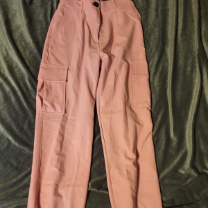 Rosa cargopants från Bershka - Säljer ett par snygga rosa cargopants från Bershka. Byxorna har flera praktiska fickor och elastiska muddar vid bensluten för en bekväm passform. Perfekta för en avslappnad stil.