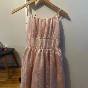 Ljusrosa klänning med spetsdetaljer - Charmig ljusrosa klänning med tunna axelband och vacker spetsdetaljering. Perfekt för somriga tillfällen med sin luftiga design och eleganta look. 