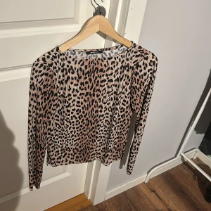 Leopardmönstrad topp från Gina Tricot - Snygg leopardmönstrad topp från Gina Tricot i beige och svart med silkestyg. Toppen har långa ärmar och är perfekt för att ge din outfit en trendig touch. Passar bra till både jeans och kjol. 