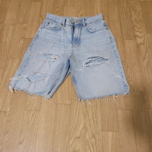 Ljusa jeansshorts  - Säljer ett par ljusa jeansshorts från gina tricot med slitna detaljer och fransig kant. Perfekta för en avslappnad stil. De har en klassisk femficksdesign och knappgylf.
