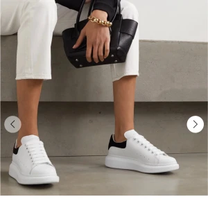 Vita sneakers med svart detalj - Stilrena vita sneakers med svart häl från Alexander McQueen. Skorna har en tjock sula och klassisk snörning. Perfekta för en modern och minimalistisk look.