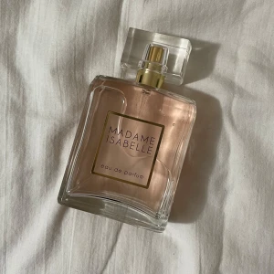 Madame Isabelle Eau de Parfum - Elegant och sofistikerad parfym i en stilren glasflaska med en ljusrosa doftvätska. Perfekt för den som söker en klassisk och tidlös doft. 