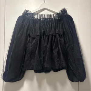 Svart offshoulder blus - Elegant svart offshoulder blus med volangdetaljer. Tillverkad i ett lätt och luftigt material som ger en romantisk känsla. Perfekt för en stilfull look.