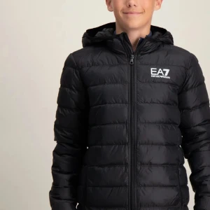 Svart pufferjacka från EA7 - Snygg svart pufferjacka från EA7 med dragkedja och huva. Perfekt för kyliga dagar. Jackan har en stilren design med logotyp på bröstet.