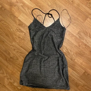 Glittrig klänning med tunna axelband - Snygg glittrig klänning i mörk silver med tunna axelband och v-ringad design. Perfekt för en festlig kväll med sin glittriga yta och eleganta passform.