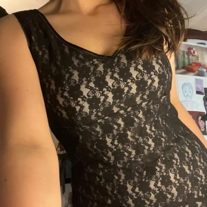 Svart spetsklänning - Elegant svart klänning i spets med v-ringad hals och ärmlös design. Perfekt för festliga tillfällen med sin klassiska och stilrena look. Har en underklänning i ljusfärg och en fin modell hade kunnat funka till bal eller liknande.