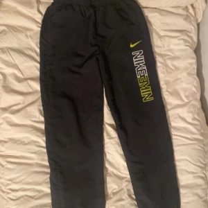 Svarta träningsbyxor från Nike - !står XL på storlek men den är liten i sin storlek och passar M/L!     Säljer ett par svarta träningsbyxor från Nike med elastisk midja och logga i vitt och gult på benet. Byxorna har en sportig look och är perfekta för träning eller avslappnade dagar. De har även dragkedjor vid bensluten för justerbar passform. 