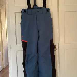 Skidbyxor från Five Seasons - Snygga blå och svarta skidbyxor från Five Seasons med hängslen. Perfekta i skid- eller pulkabacken i slitstarkt material för att klara kalla dagar. Mycket bra skick, har bara använts en säsong då tonåringen har vuxit ur dem. 