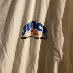 Vit t-shirt från Driveway Paradise - Säljer en vit t-shirt från Driveway Paradise med tryck i blått och orange på bröstet. T-shirten är tillverkad i bomull med inslag av viskos och elastan för extra komfort. Perfekt för en avslappnad stil.