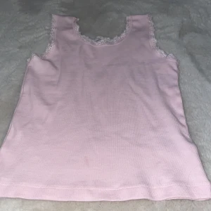 Rosa ribbad linnetopp med spetsdetaljer - Söt rosa ribbad linnetopp från 157 med fina spetsdetaljer runt halsringningen och ärmhålen. Perfekt för en avslappnad och feminin stil.