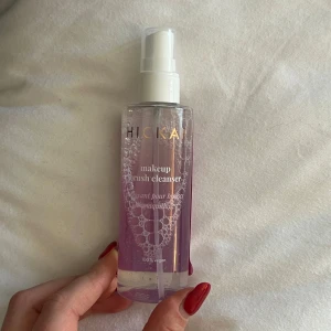 Makeup Brush Cleanser från Hickap - Säljer en makeup brush cleanser från Hickap. Den kommer i en genomskinlig flaska med pump och innehåller en lila vätska. Perfekt för att hålla dina sminkborstar rena och fräscha. Produkten är 100% vegansk.