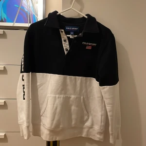 Tröja från Polo Sport Ralph Lauren - Stilren svart och vit tröja från Polo Sport Ralph Lauren. Tröjan har en krage med knappar och en stor ficka framtill. Märkesloggan syns både på bröstet och längs ärmen. Den är inte använd särskilt mycket och har ett väldigt fint skick. Listpris: 1095 kr men jag säljer den för 550 kr. Tröjan har storlek 10-12 eller M. 