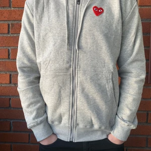 CDG zipup - Säljer en ljusgrå zipup hoodie av märket CDG/Comme des cargons. Den är i helt nytt skick och har lapparna kvar på. Storlek M