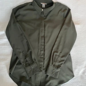 Olivgrön skjorta från H&M - Snygg olivgrön skjorta från H&M i storlek S. Skjortan har långa ärmar och en klassisk krage med knappar framtill. 