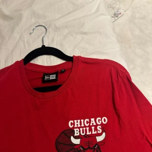 Röd Chicago Bulls t-shirt från New Era - Snygg röd t-shirt från New Era med Chicago Bulls-logga på både fram- och baksidan. Perfekt för basketfans som vill visa sitt stöd för laget. T-shirten är kortärmad och tillverkad i bomull för en bekväm passform. storlek S från herr, köpt i JD sports. skriv vid intresse!!
