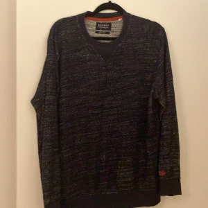 Mörkblå stickad tröja från Esprit - Snygg mörkblå stickad tröja från Esprit i slim fit. Tröjan har en diskret v-ringning och ett litet broderat märke på ärmen. Perfekt för kyliga dagar.