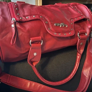 Röd vintage bag i Skinn från Björn Borg! - Rymlig och snygg röd vintage bag i skinn med dekorativa nitar, snygga detaljer samt både handtag och justerbar axelrem.  Mått: 35 x 20 cm. Inga skador eller slitningar finns. Originell och snygg!        OBS! Tar inga bilder med väskan. För bilder eller annat som mot förmodan inte framgår i annonsen specificera på vad! 