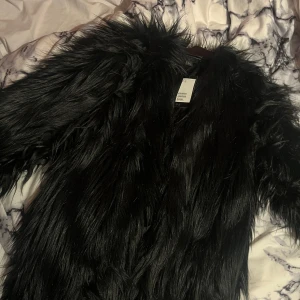 Svart pälsjacka - Snygg svart pälsjacka med långärmad design. Perfekt för att hålla sig varm och stilren under kyliga dagar. Jackan har en fluffig textur som ger en lyxig känsla. Helt oanvänd, prislappen sitter kvar. Köpt för 800 kronor.