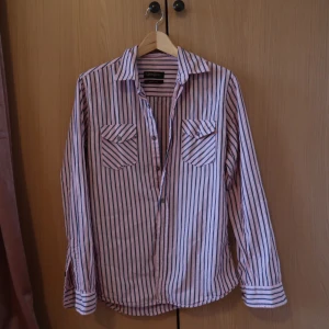 Randig skjorta från William Baxter - Snygg randig skjorta från William Baxter i rosa och blått. Skjortan har långa ärmar och knappar framtill samt två bröstfickor med knappstängning. Perfekt för en stilren look.