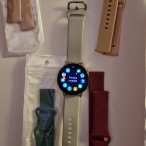 Samsung Galaxy Watch Active2 - Säljer en Samsung Galaxy Watch Active2 med flera utbytbara armband i olika färger. Klockan har en rund skärm och ett stilrent gränssnitt. Perfekt för den som vill hålla koll på sin träning och hälsa.