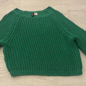 Grön stickad tröja från H&M - Säljer en snygg grön stickad tröja från H&M. Tröjan har en klassisk rund hals och långa ärmar, perfekt för kyligare dagar. Den är i en härlig grön färg som livar upp garderoben.