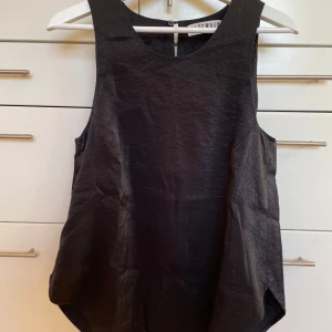 Svart ärmlös topp från Altewaisaome - Snygg svart ärmlös topp från Altewaisaome med rund halsringning i viskos. Materialet har en lätt glansig finish som ger en elegant touch. Perfekt skick! Storlek 42 men passar storlek 38 och uppåt.