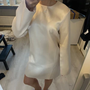 Beige klänning med lång ärm - Elegant beige klänning med lång ärm och enkel design. Perfekt för en stilren look. Klänningen har en rak passform och är tillverkad i ett mjukt material.