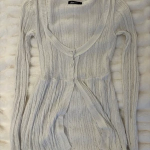 Vit babydoll kofta - Mysig vit stickad babydoll kofta från Gina Tricot i storlek XS. Koftan har ett flätatmösnter och tre knappar vid midjan