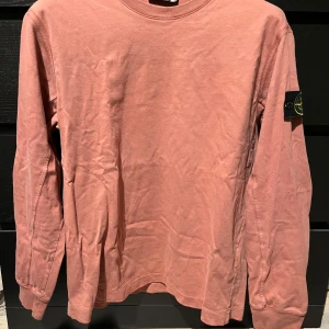 Långärmad tröja från Stone Island - Säljer en snygg rosa långärmad tröja från Stone Island. Tröjan har en rund halsringning och det ikoniska Stone Island-märket på ärmen. Perfekt för en avslappnad stil. Tröjan är äkta och det finns inget kvitto. Den är i storlek L och är knappt använd. 