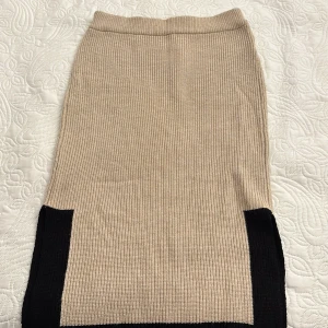 Beige stickad kjol från Lindex - Snygg beige stickad kjol från Lindex med svarta detaljer längst ner. Kjolen är gjord av LENZING™ ECOVERO™ viskosblandning, vilket gör den både bekväm och hållbar. Använd inte ens 5 gånger!