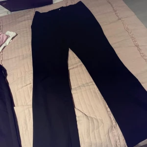 Svarta kostymbyxor med hög midja - Snygga svarta kostymbyxor med hög midja och elastisk linning. Byxorna har en stilren design med knappar framtill och raka ben. Perfekta för en elegant look.