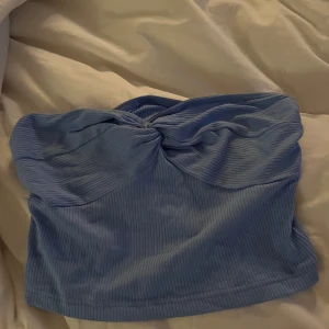 Blå ribbad tubtopp - Snygg blå ribbad tubtopp med en knutdetalj framtill. Perfekt för sommardagar eller en utekväll. Enkel att matcha med olika outfits.